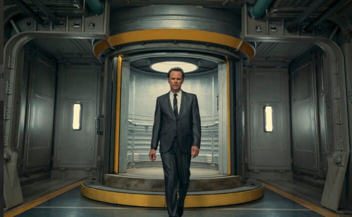 A screenshot from Fallout Season One showing Cooper Howard in a sharp suit walking through a Vault